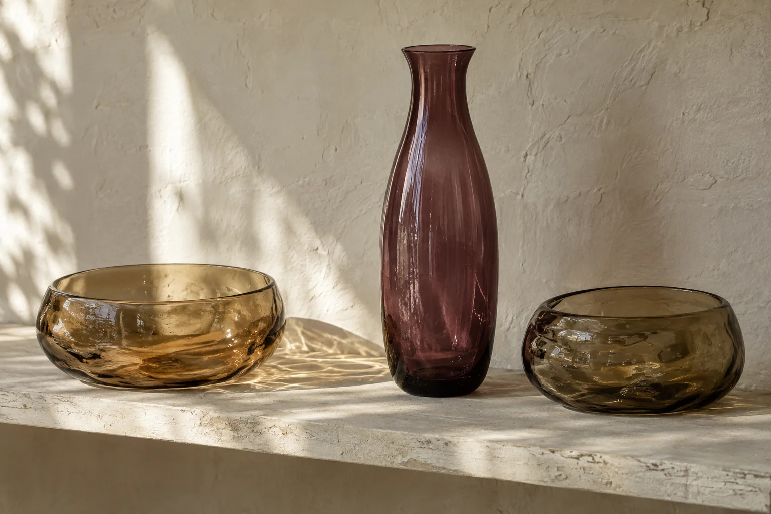 Amber bowls and a plum glass vase spaced across a pale shelf.